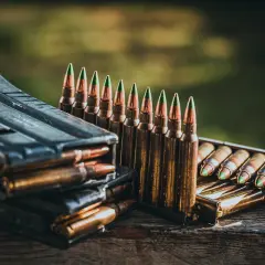 Munition im Kaliber 5,56 mm liegt bereit. Ein Magazin stapelt sich mit Patronen, daneben eine Reihe von Patronen mit grünen Spitzen.