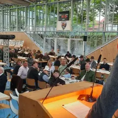 Versammlung im jagdbezirk mit mehreren revieren. Zuhörer in Tracht und Anzügen lauschen einem Vortragenden.