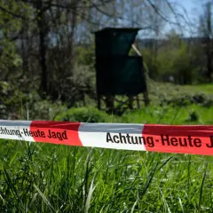 Absperrband mit der Aufschrift "Achtung - Heute Jagd" im Vordergrund. Im Hintergrund ein Hochsitz und Bäume.
