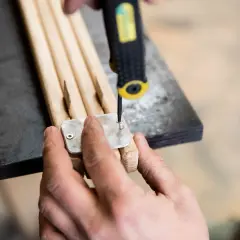 Hände schrauben eine Metallplatte an Holzstäbe, um einen zielstock selber bauen.