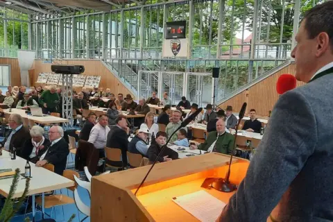 Versammlung im jagdbezirk mit mehreren revieren. Zuhörer in Tracht und Anzügen lauschen einem Vortragenden.