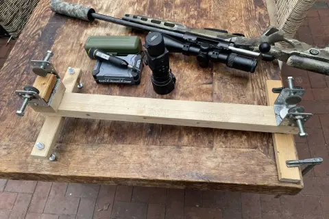 Selbstgebaute Gewehrauflage aus Holz und Metallteilen, daneben ein Jagdgewehr mit Schalldämpfer, Zielfernrohr und Wärmebildgerät.