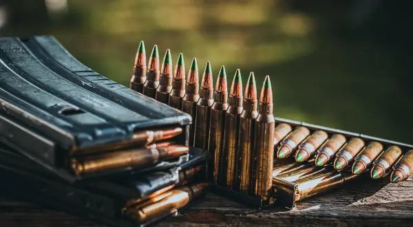 Munition im Kaliber 5,56 mm liegt bereit. Ein Magazin stapelt sich mit Patronen, daneben eine Reihe von Patronen mit grünen Spitzen.