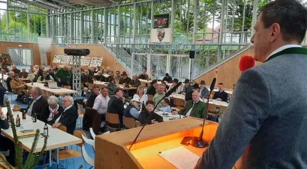 Versammlung im jagdbezirk mit mehreren revieren. Zuhörer in Tracht und Anzügen lauschen einem Vortragenden.