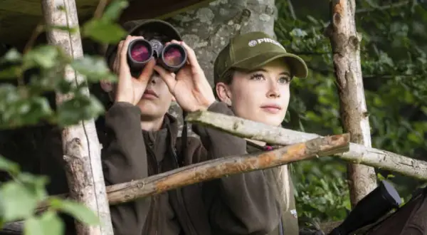 Zwei junge Jagdscheininhaber in Deutschland blicken aus einem Hochsitz in den Wald.
