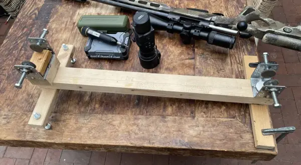 Selbstgebaute Gewehrauflage aus Holz und Metallteilen, daneben ein Jagdgewehr mit Schalldämpfer, Zielfernrohr und Wärmebildgerät.