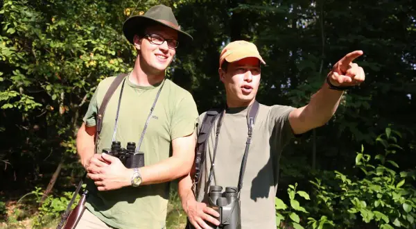 Zwei Männer mit Ferngläsern im Wald, bereit für die Jagd. Sie sind Teil des Landesjagdverbands Hamburg.