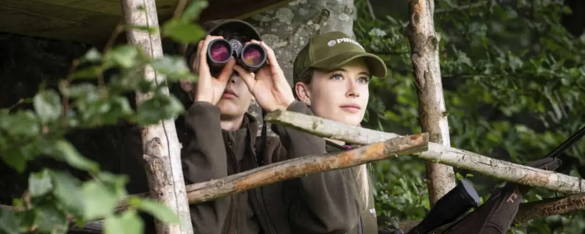 Zwei junge Jagdscheininhaber in Deutschland blicken aus einem Hochsitz in den Wald.