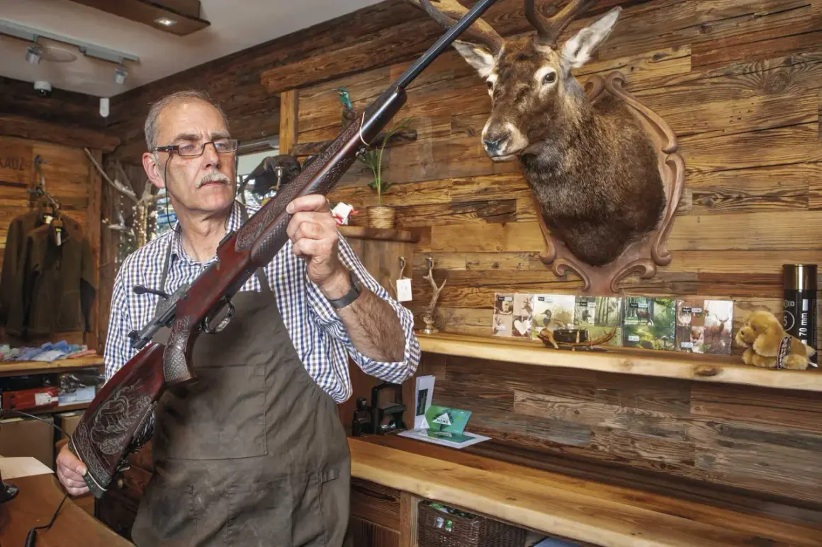 Ein Mann prüft eine Blaser R8 Büchse, vielleicht wegen Blaser R8 Verschluss Probleme. Ein Hirschkopf hängt an der Wand.
