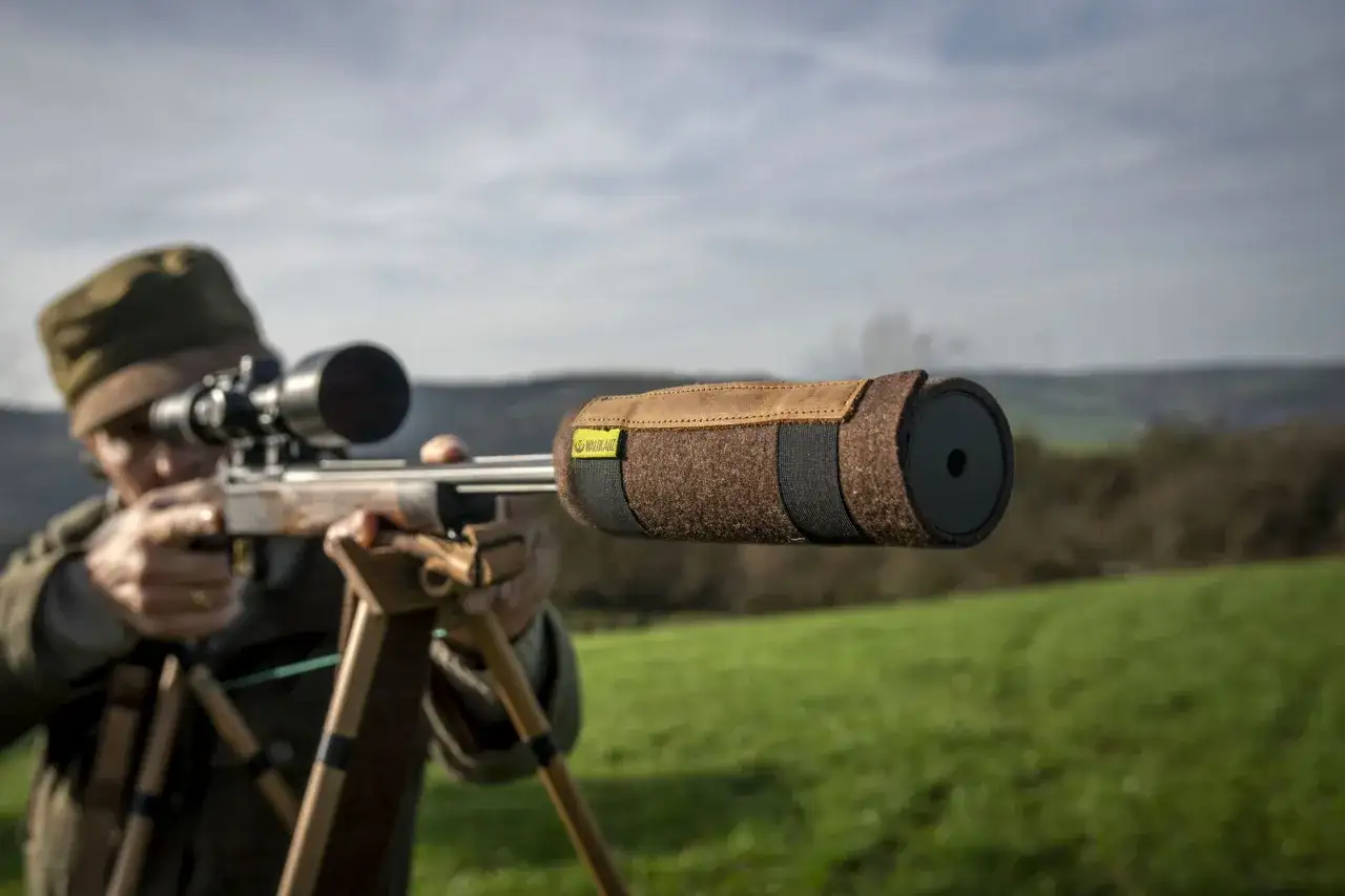 Jäger zielt mit einem Gewehr mit kurzem Lauf und Schalldämpfer-Schutzhülle auf ein Feld.