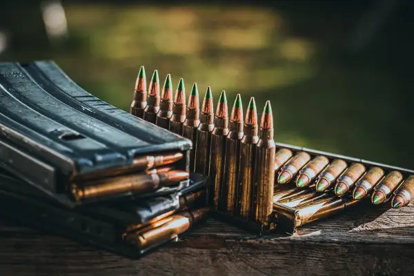 Munition im Kaliber 5,56 mm liegt bereit. Ein Magazin stapelt sich mit Patronen, daneben eine Reihe von Patronen mit grünen Spitzen.