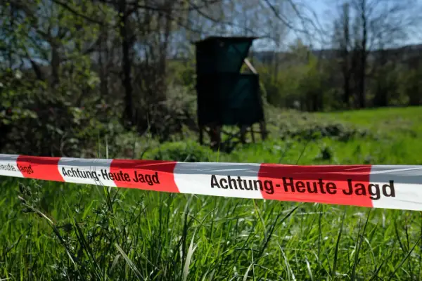 Absperrband mit der Aufschrift "Achtung - Heute Jagd" im Vordergrund. Im Hintergrund ein Hochsitz und Bäume.